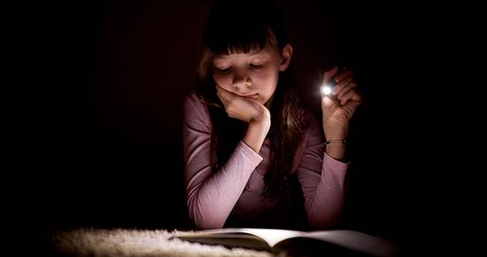 女孩在黑暗中拿着手电筒看书